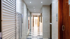 Un couloir au sol carrelé, une porte en bois sur la droite et un panneau indiquant la direction des toilettes.
