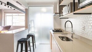 Une cuisine moderne avec un coin bar, une cuisinière à gaz et un évier. On y trouve deux tabourets et une fenêtre qui laisse entrer la lumière naturelle.