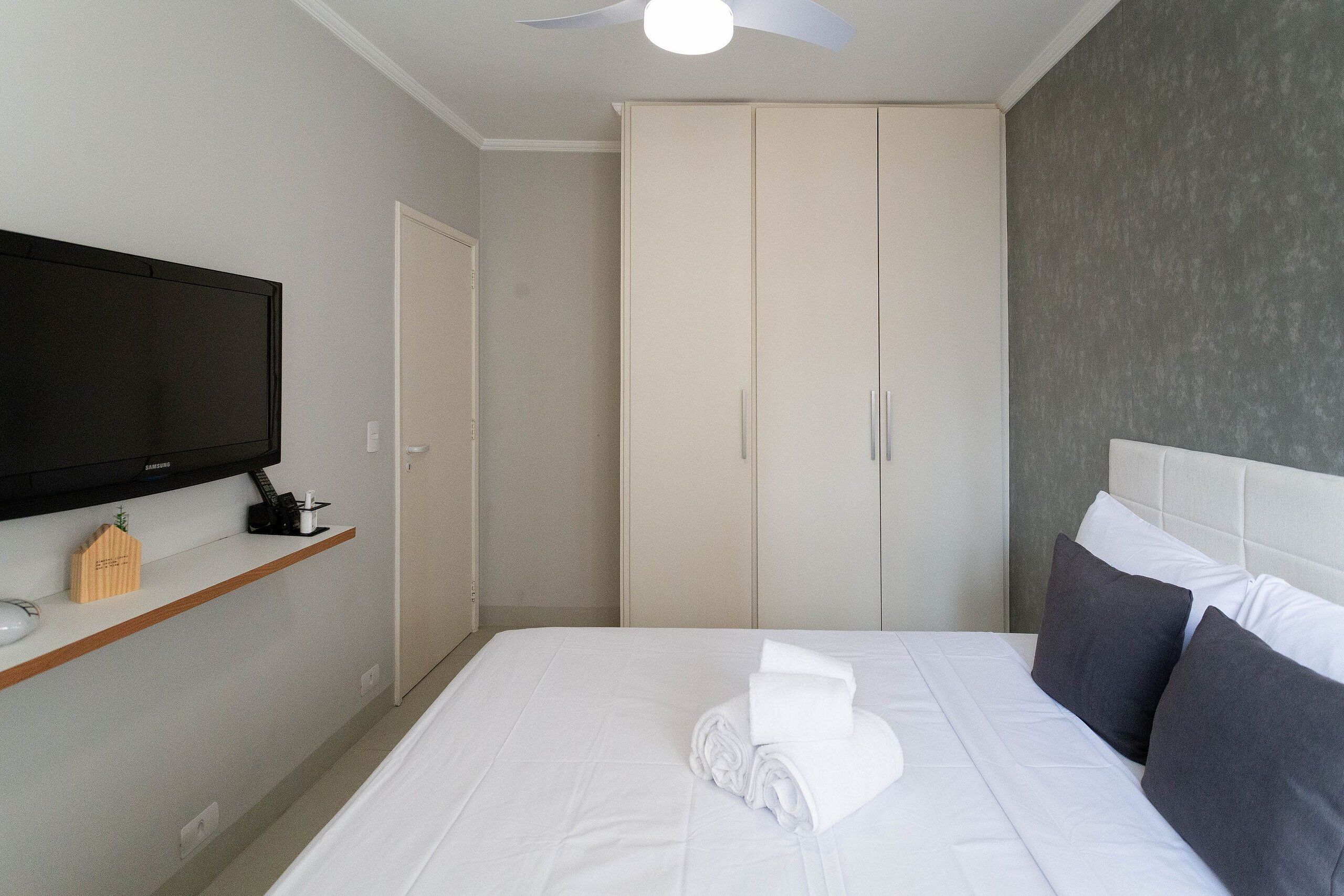 A hotel room with a bed, a television on a shelf, and a wardrobe.