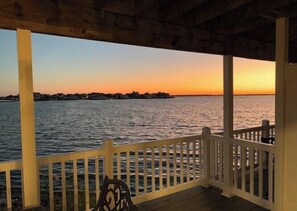 A wooden deck with a white railing overlooking a body of water during sunset. - Seas The Bay on the Waterfront! (Ocean City)