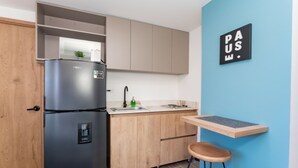 Una cocina compacta con un refrigerador negro, armarios de madera, un lavamanos y un taburete pequeño.