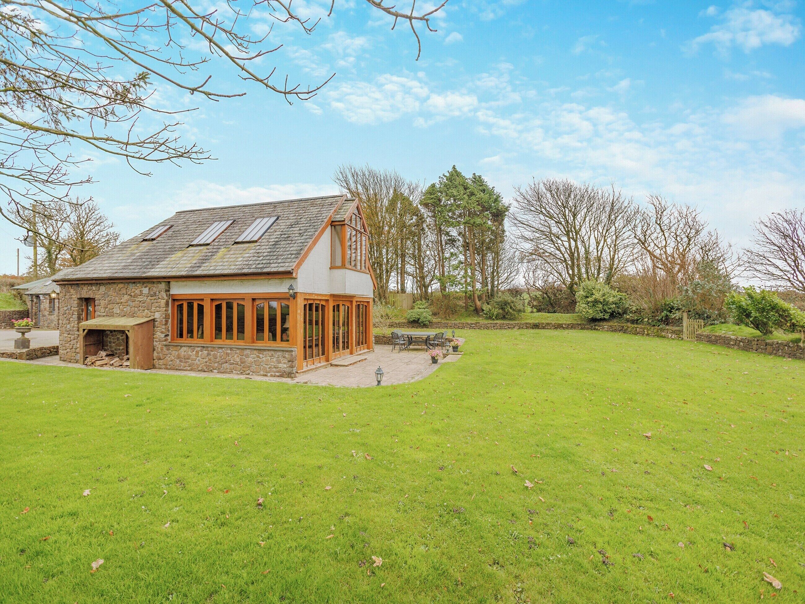 A stone house with a sloped roof, large windows, and a grassy yard.