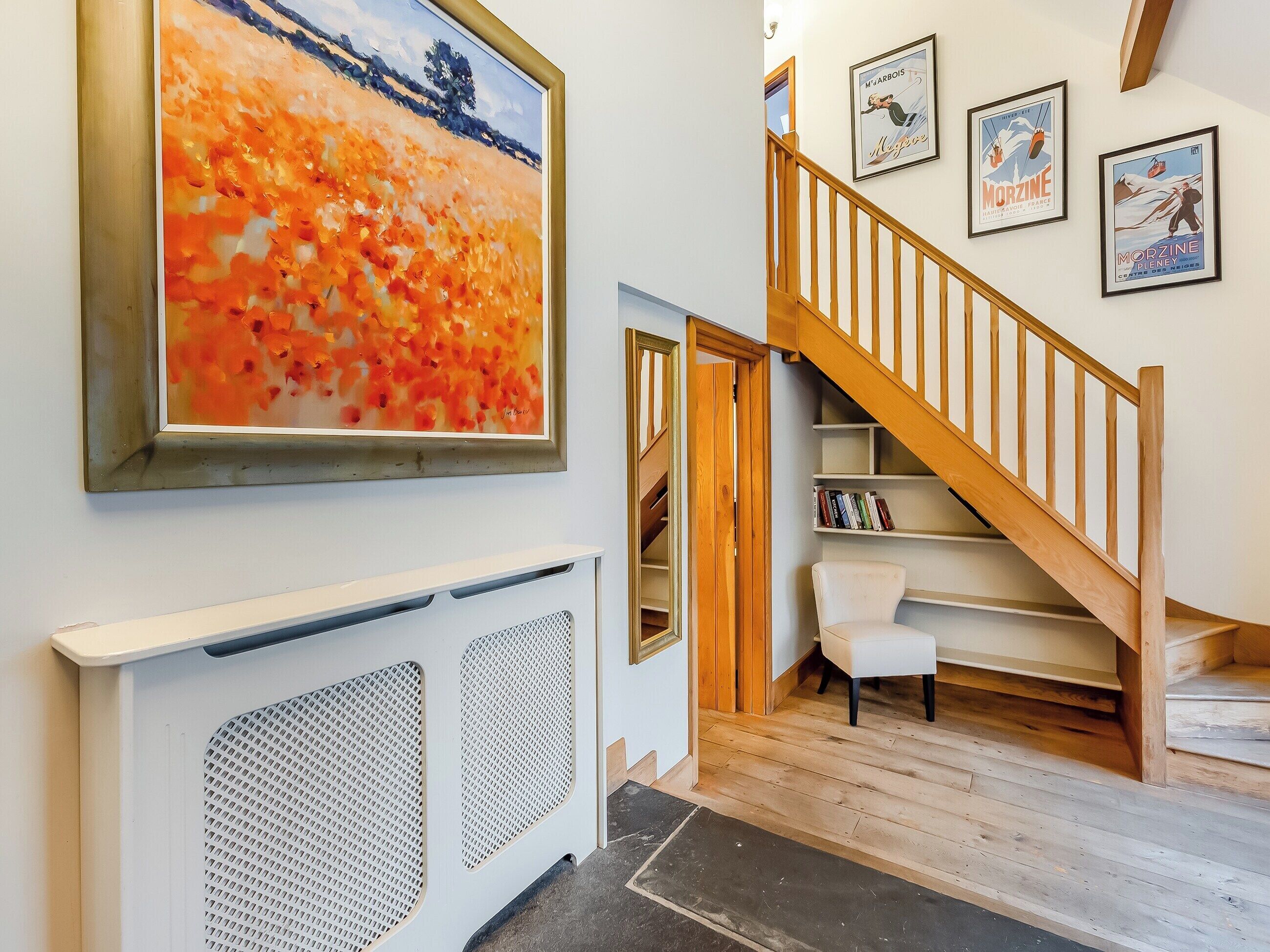 A staircase with wooden railings leading to a landing with a white chair and bookshelves.