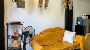Une pièce comprenant un canapé en bois, un panier tressé, un ventilateur et des objets décoratifs suspendus.