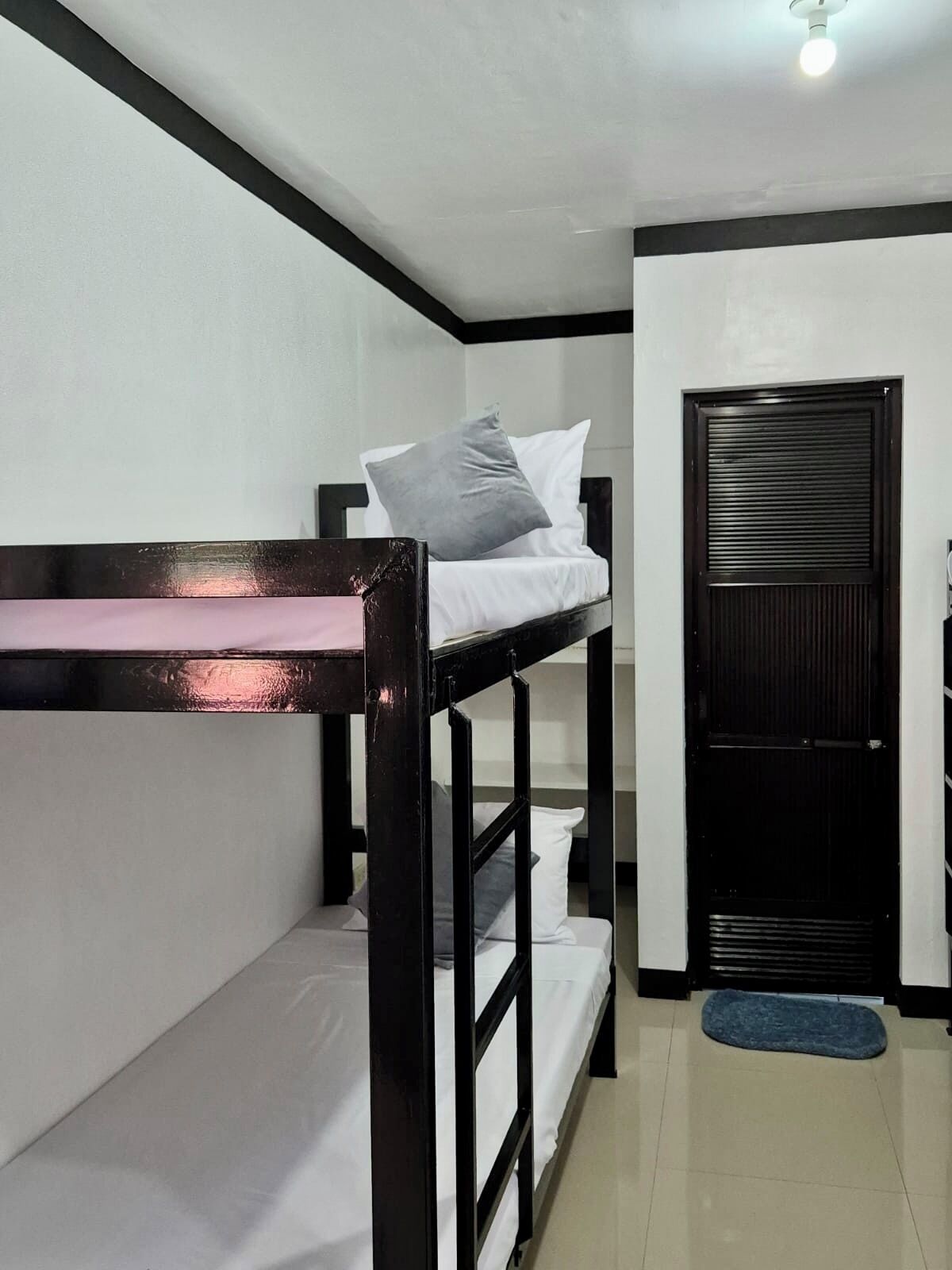 Een slaapkamer met stapelbedden, een zwarte deur en een kleed op de vloer.