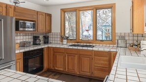 Une cuisine moderne avec des meubles en bois, un réfrigérateur en acier inoxydable, un four à micro-ondes et une fenêtre donnant sur l’extérieur.