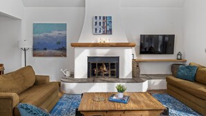 Un salon avec une cheminée, deux canapés, une table basse et des œuvres d’art accrochées aux murs.