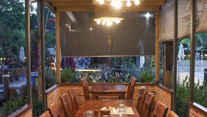 An outdoor dining area with a long wooden table set for six, surrounded by brick walls and large windows. - NV Sport Camp & Hotel - Ho Tram (Ho Chi Minh City)