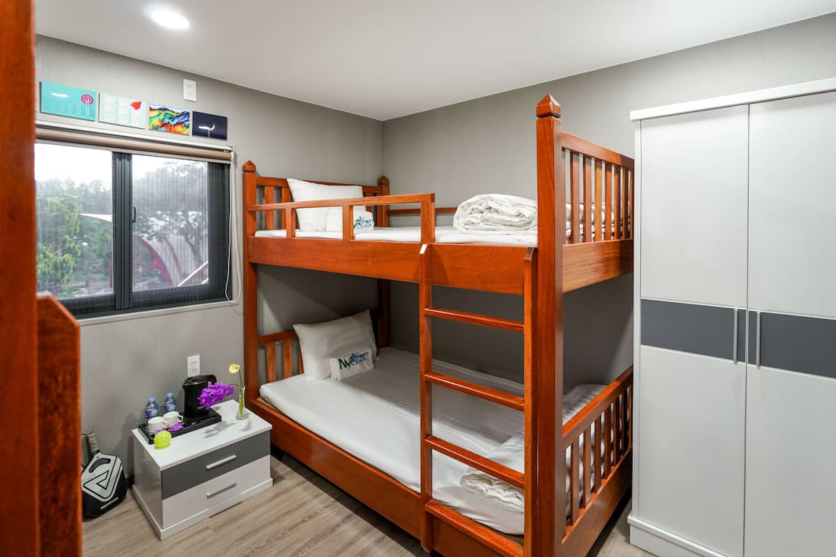 A bunk bed room with a window, a small bedside table, and a wardrobe.