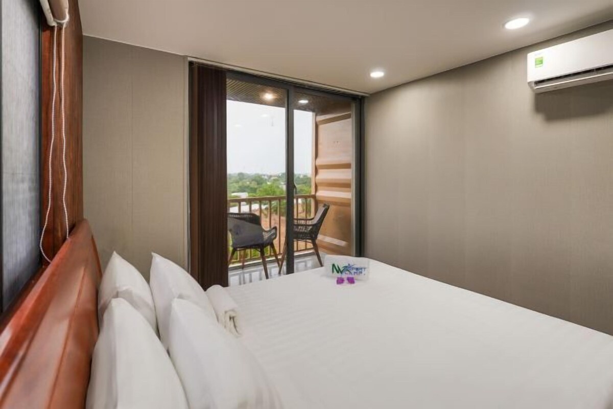 A hotel room with a bed, a window, and a balcony with chairs.