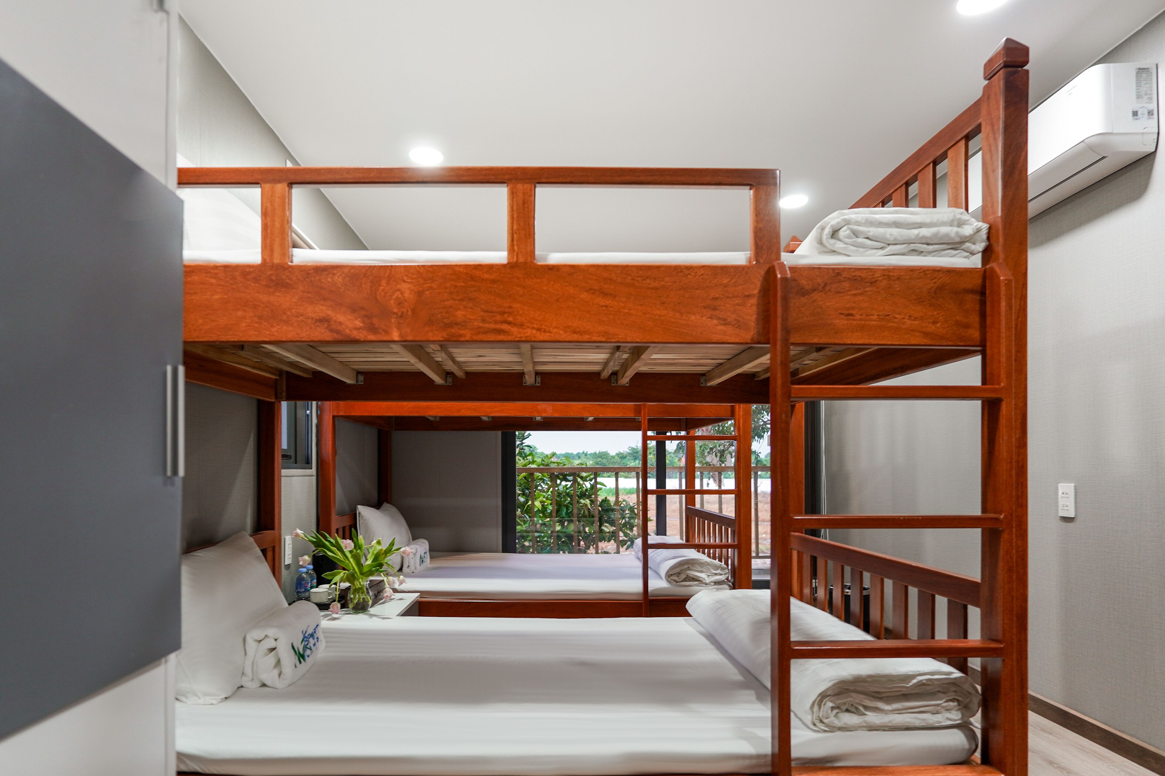 A bunk bed room with a balcony, a small table with a plant, and a white wall with an air conditioning unit.