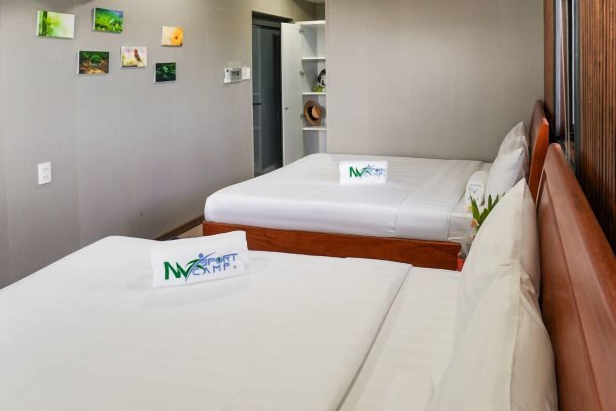A hotel room with two beds, a wooden headboard, a small shelf with decorative items, and a wall with framed pictures.