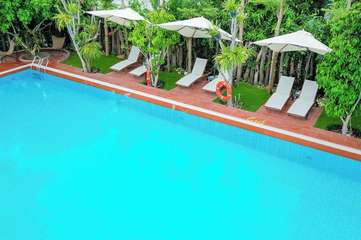 A swimming pool with lounge chairs and umbrellas, surrounded by greenery.