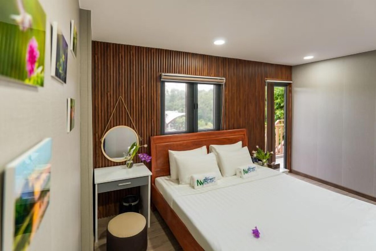 A modern bedroom with a wooden headboard, a large bed with white bedding, a bedside table with a mirror, and a small stool.