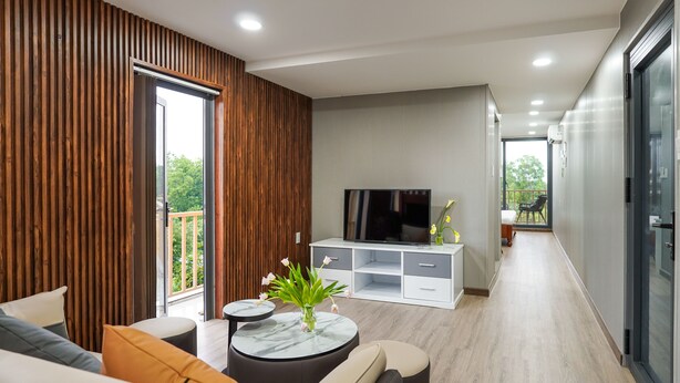 A modern living room with a sofa, a round coffee table, a TV, and a balcony. - NV Sport Camp & Hotel - Ho Tram (Ho Chi Minh City)