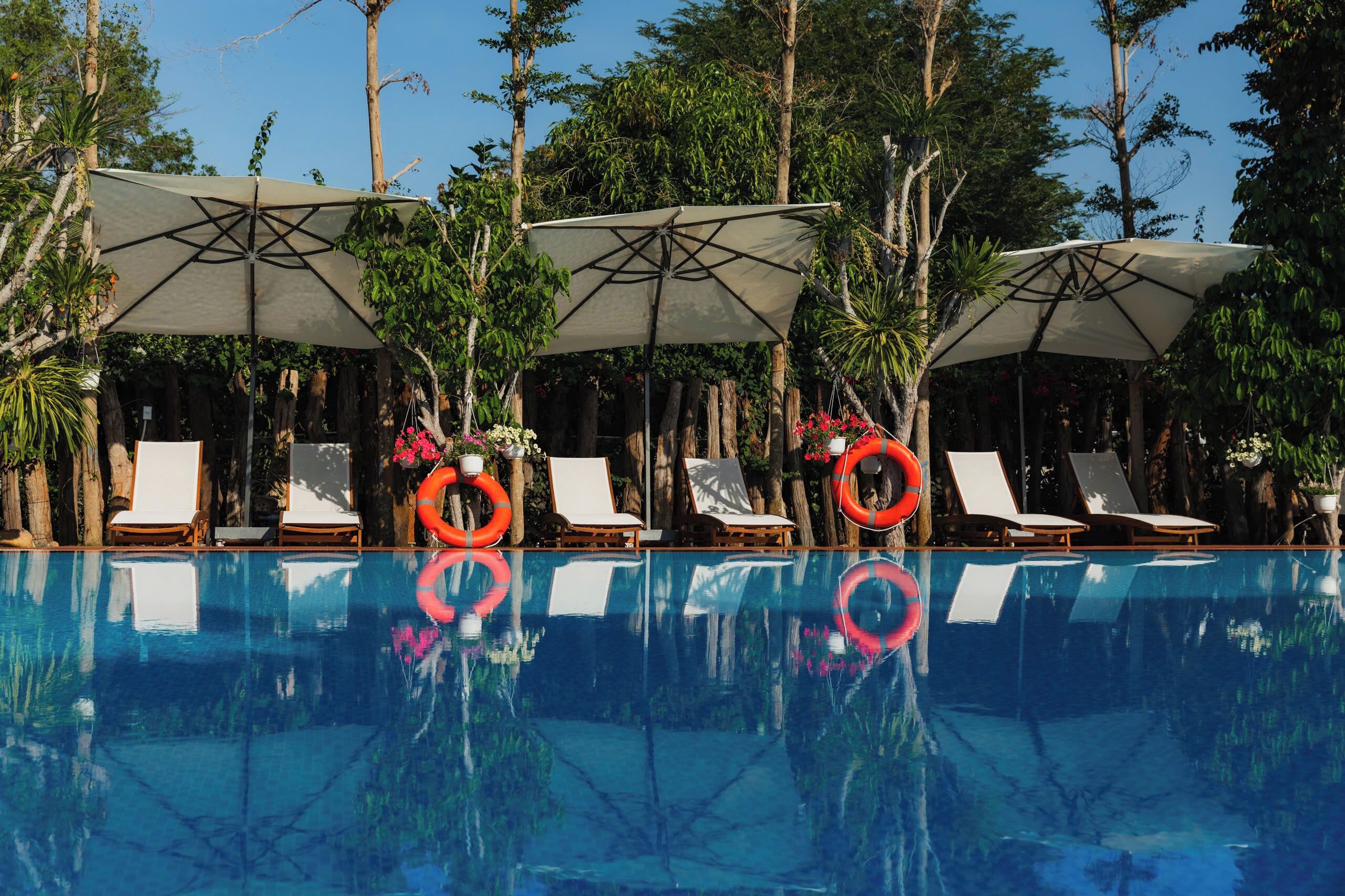 Zona de piscina con sillas de descanso, sombrillas y boyas salvavidas.