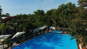 A swimming pool with clear blue water, surrounded by trees and umbrellas. - NV Sport Camp & Hotel - Ho Tram (Ho Chi Minh City)