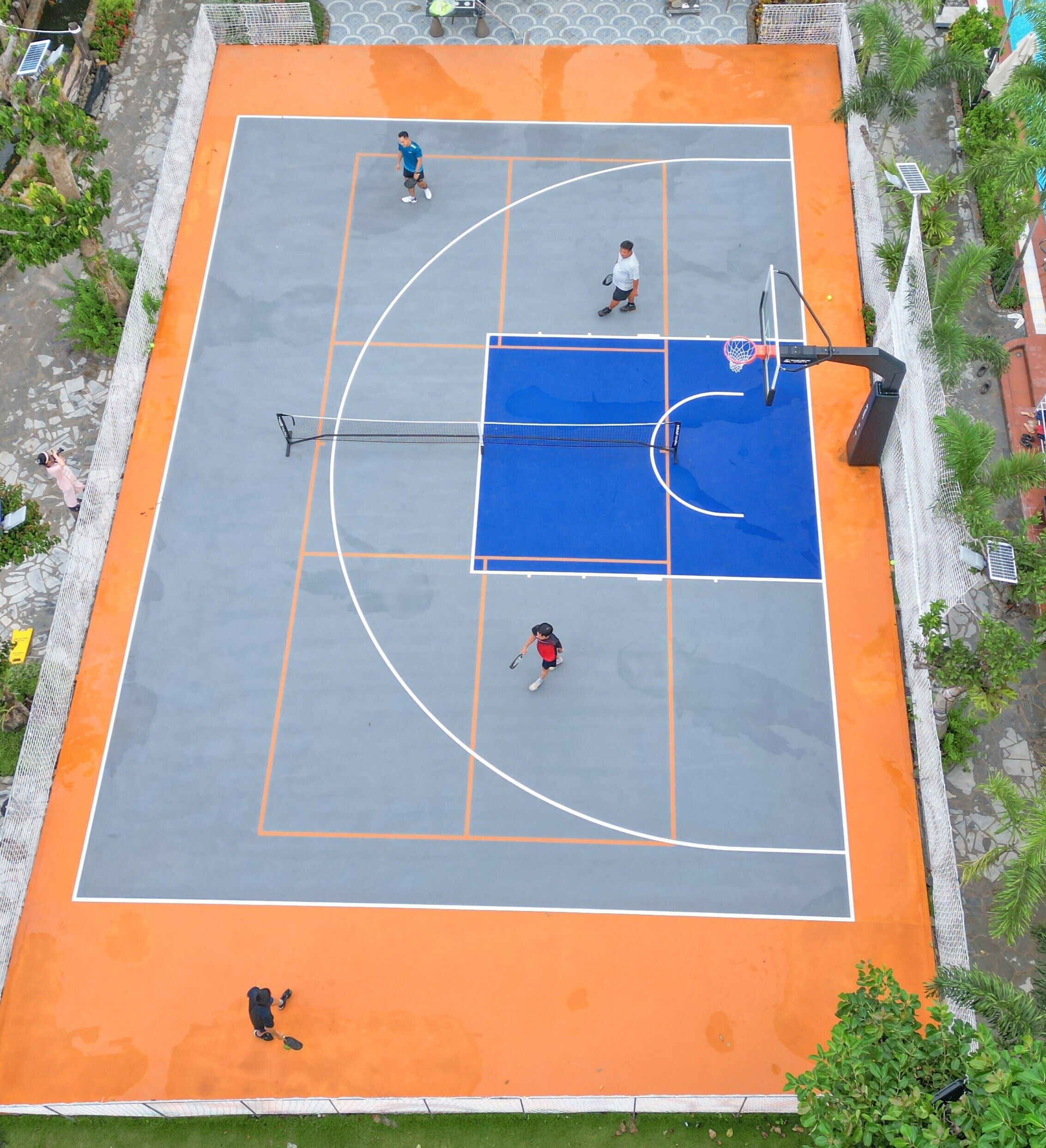 An outdoor basketball court with a blue playing area and orange borders.