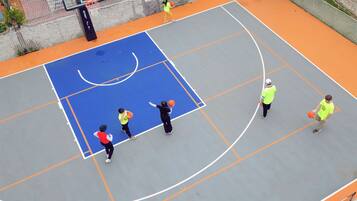 An outdoor basketball court with a blue and orange playing surface, surrounded by a white fence.