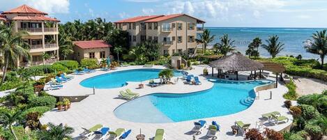 A resort with a large central pool, multiple lounge areas with sunbeds, and a view of the ocean.