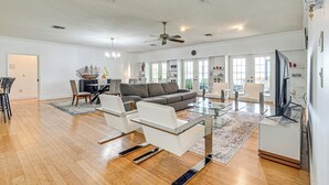 A spacious living room with a gray sofa, white chairs, a glass coffee table, and a flat-screen TV. - Waterfront Home w/ Boat Dock in Lake Placid! (Lake Placid)
