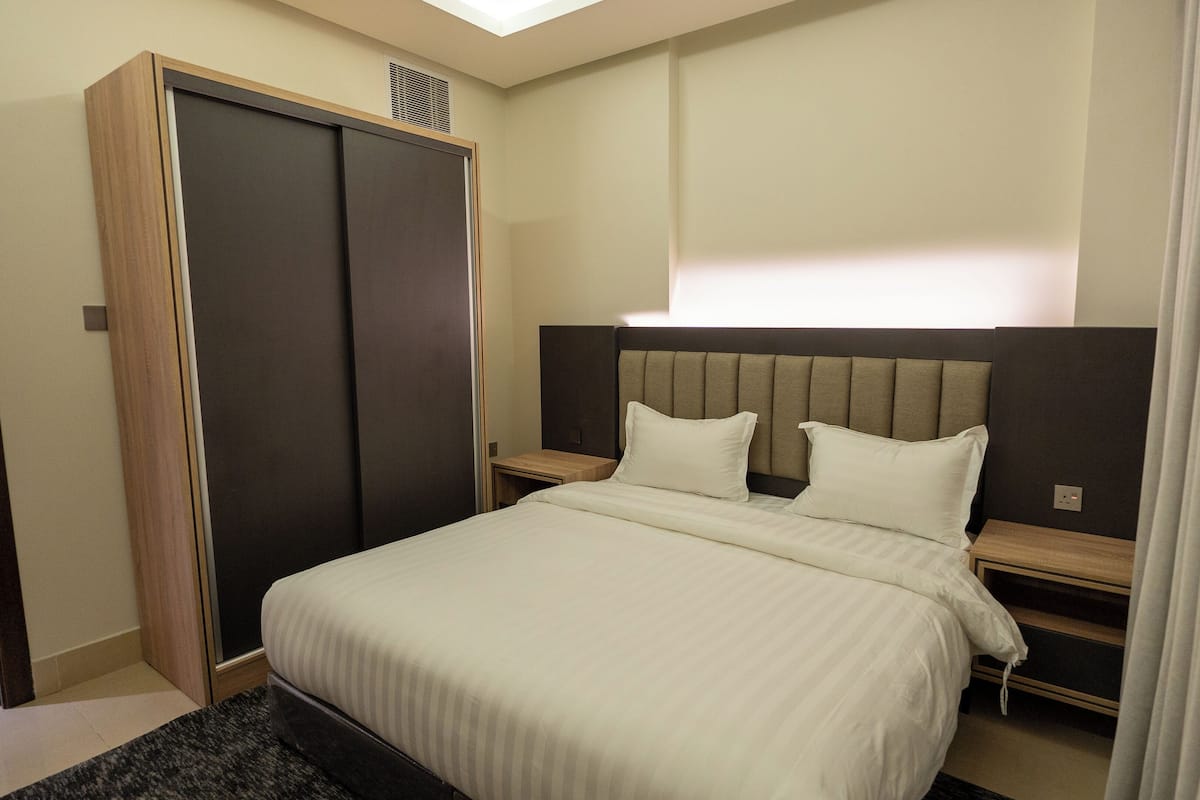 Une chambre d’hôtel avec un grand lit, une armoire, une table de chevet et une petite table de nuit.