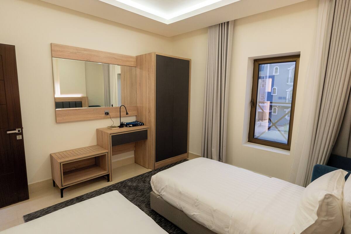 Une chambre d’hôtel avec un lit, un bureau doté d’un miroir, une armoire et une fenêtre avec des rideaux.