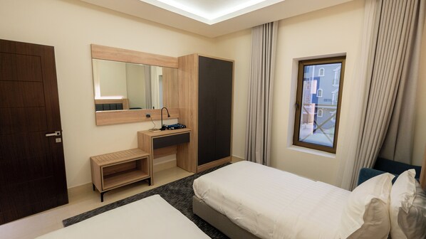 A hotel room with a bed, a desk with a mirror, a wardrobe, and a window with curtains.