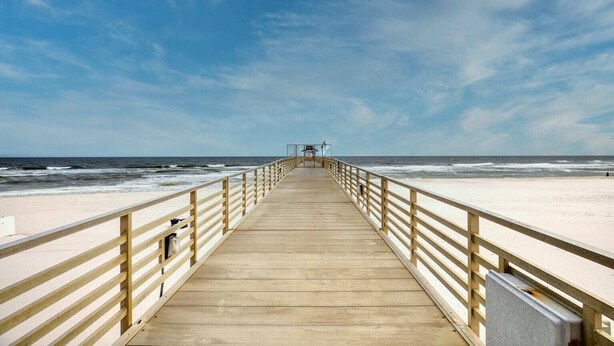 Een houten looppad dat naar een strand leidt, onder een heldere lucht.