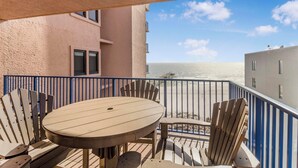 Een balkon met een ronde tafel en stoelen, met uitzicht op een strand en de oceaan.