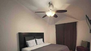 A bedroom with a bed, a ceiling fan, a nightstand, a suitcase, and a chair. - House in the Consulate! (Chihuahua)