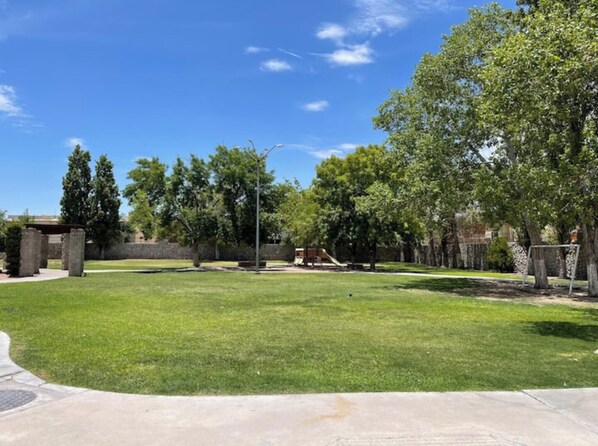 A well-maintained grassy area with a playground, trees, and a stone structure. - House in the Consulate! (Chihuahua)