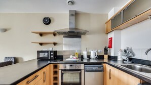 A modern kitchen with a microwave, oven, dishwasher, and stainless steel range hood. There are wooden cabinets and a black countertop.