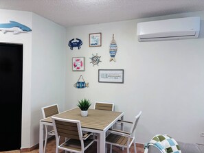 A dining area with a wooden table and white chairs, a potted plant, and nautical-themed wall decorations.