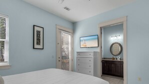 A bedroom with a bed, a dresser, a framed picture, and a door leading to a bathroom.