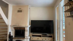 A living room with a fireplace, a television on a wooden stand, and a staircase leading to another level. - Charming duplex 4 to 6 persons Risoul 1850 (Risoul)