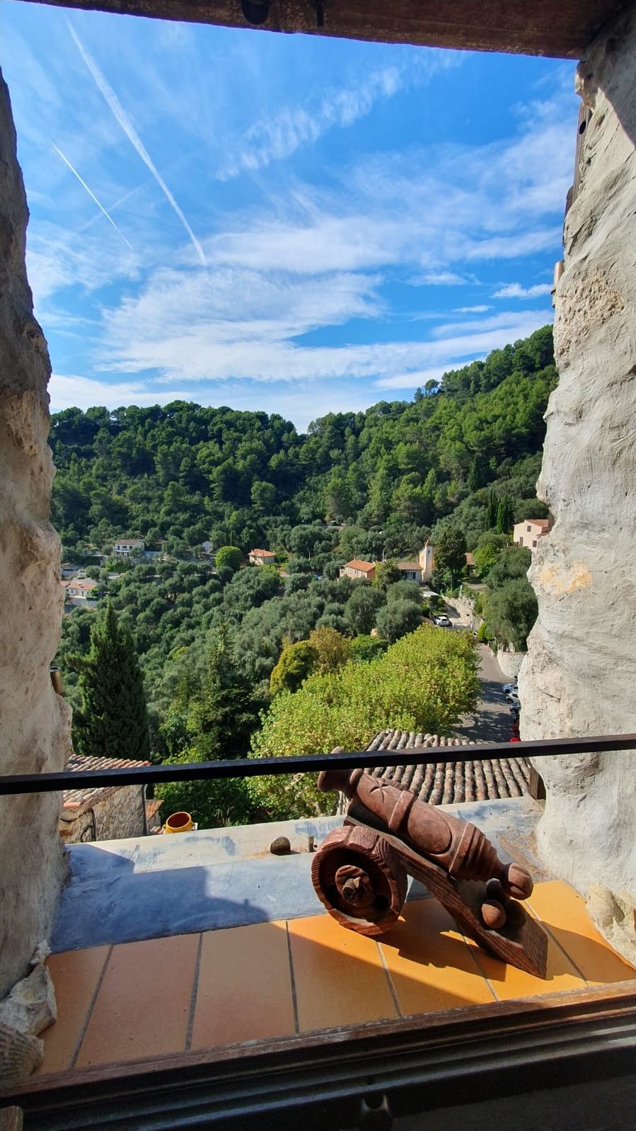 Un balcon offrant une vue sur un paysage montagneux, une sculpture rustique en bois et un sol carrelé.