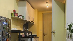 A compact kitchen with a refrigerator, a small dining table, and a potted plant.