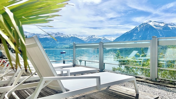 A deck with white lounge chairs overlooking a lake with a mountain backdrop. - Boutique Hotel Niesenblick Self Check In (Oberhofen am Thunersee)