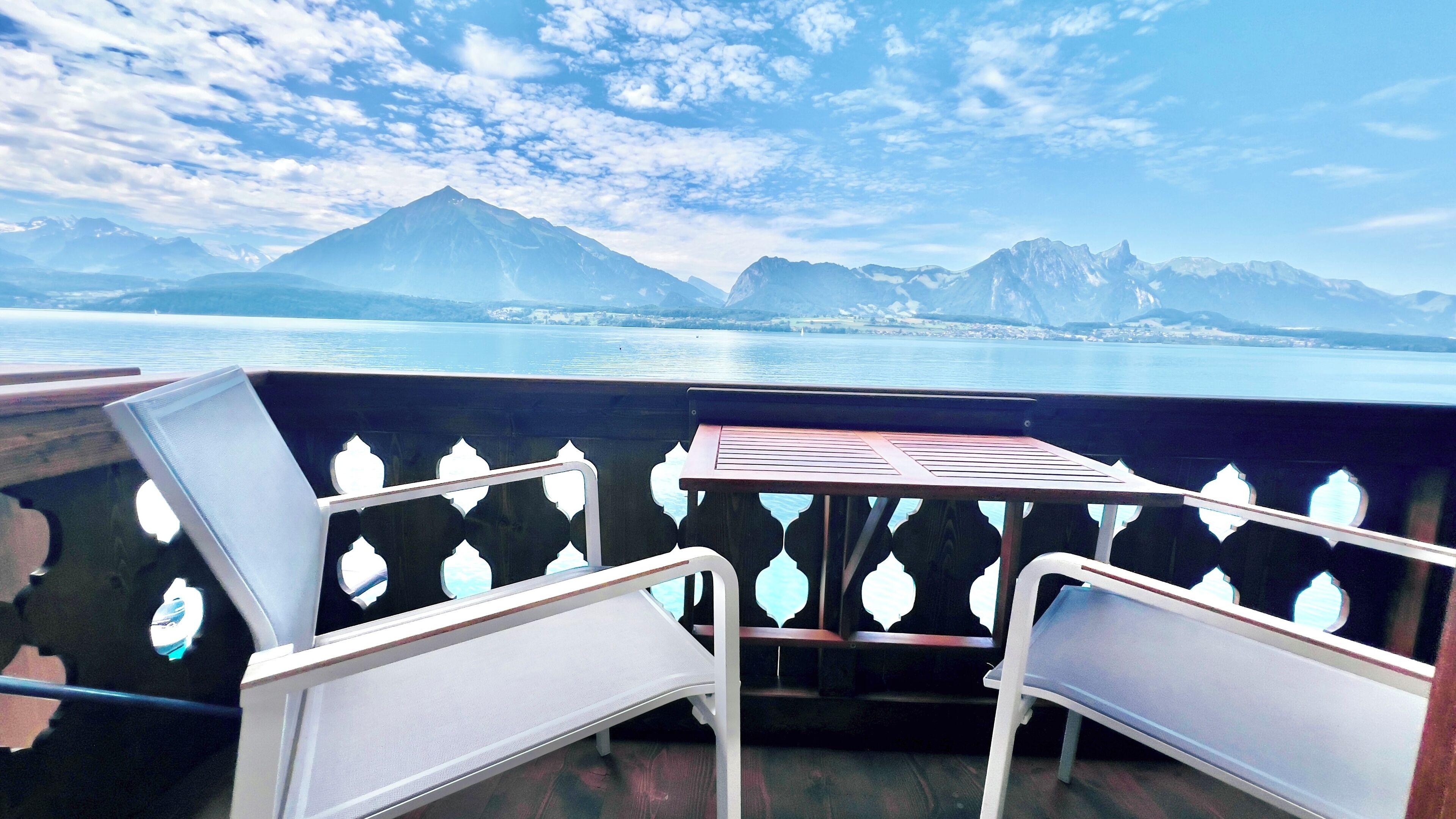 Un balcón con mesa y sillas con vistas a un lago y montañas.