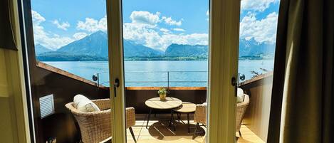 Un balcon agrémenté de meubles en osier, d’une petite table et offrant une vue sur un lac et des montagnes.