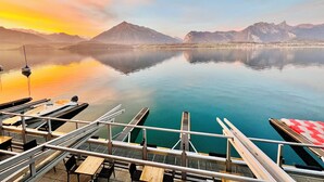 A lakeside view with a dock, boats, and mountains in the background. - Boutique Hotel Niesenblick Self Check In (Oberhofen am Thunersee)