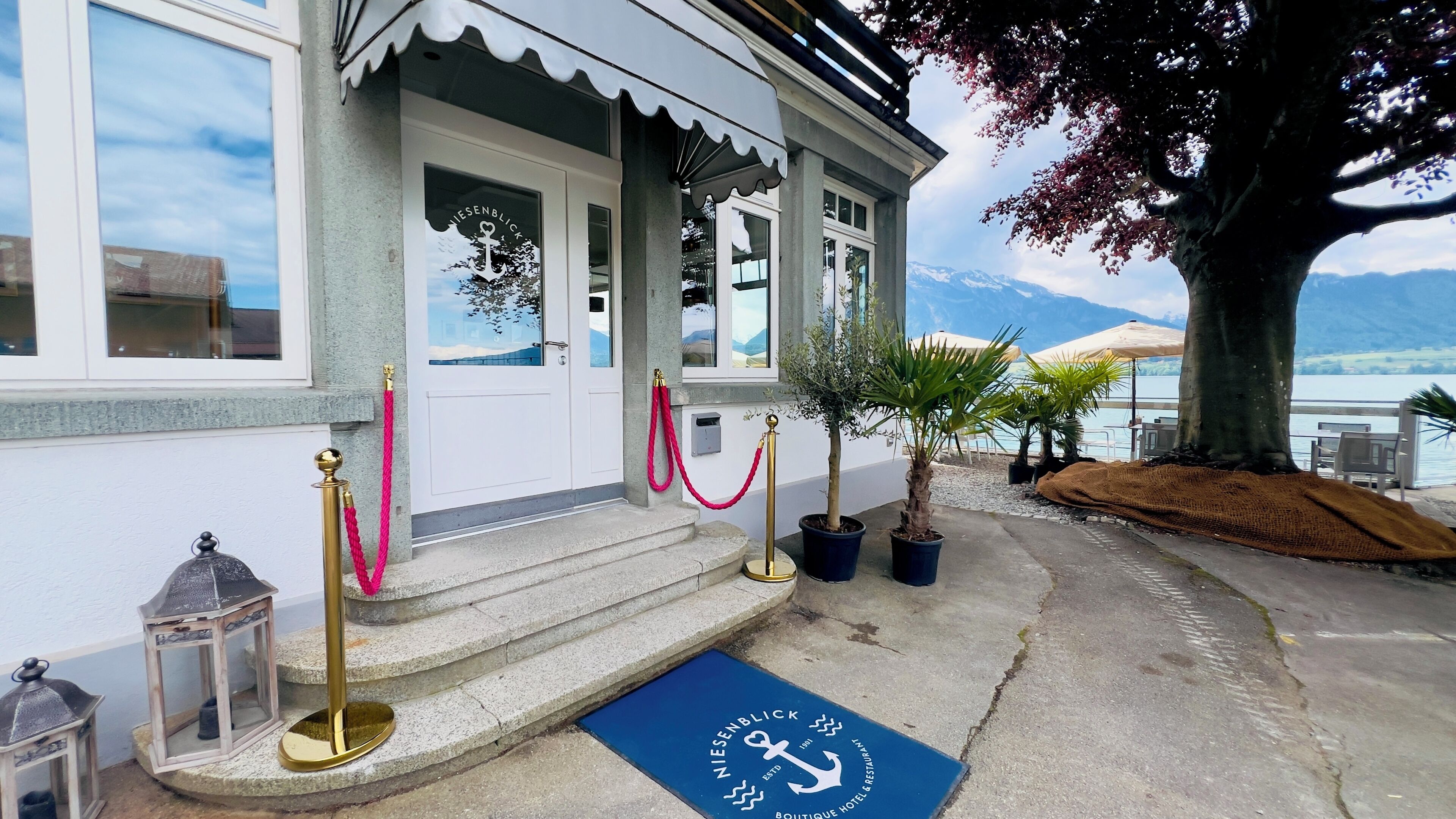 A hotel entrance with a stone staircase, a red rope barrier, and a blue mat with an anchor symbol.