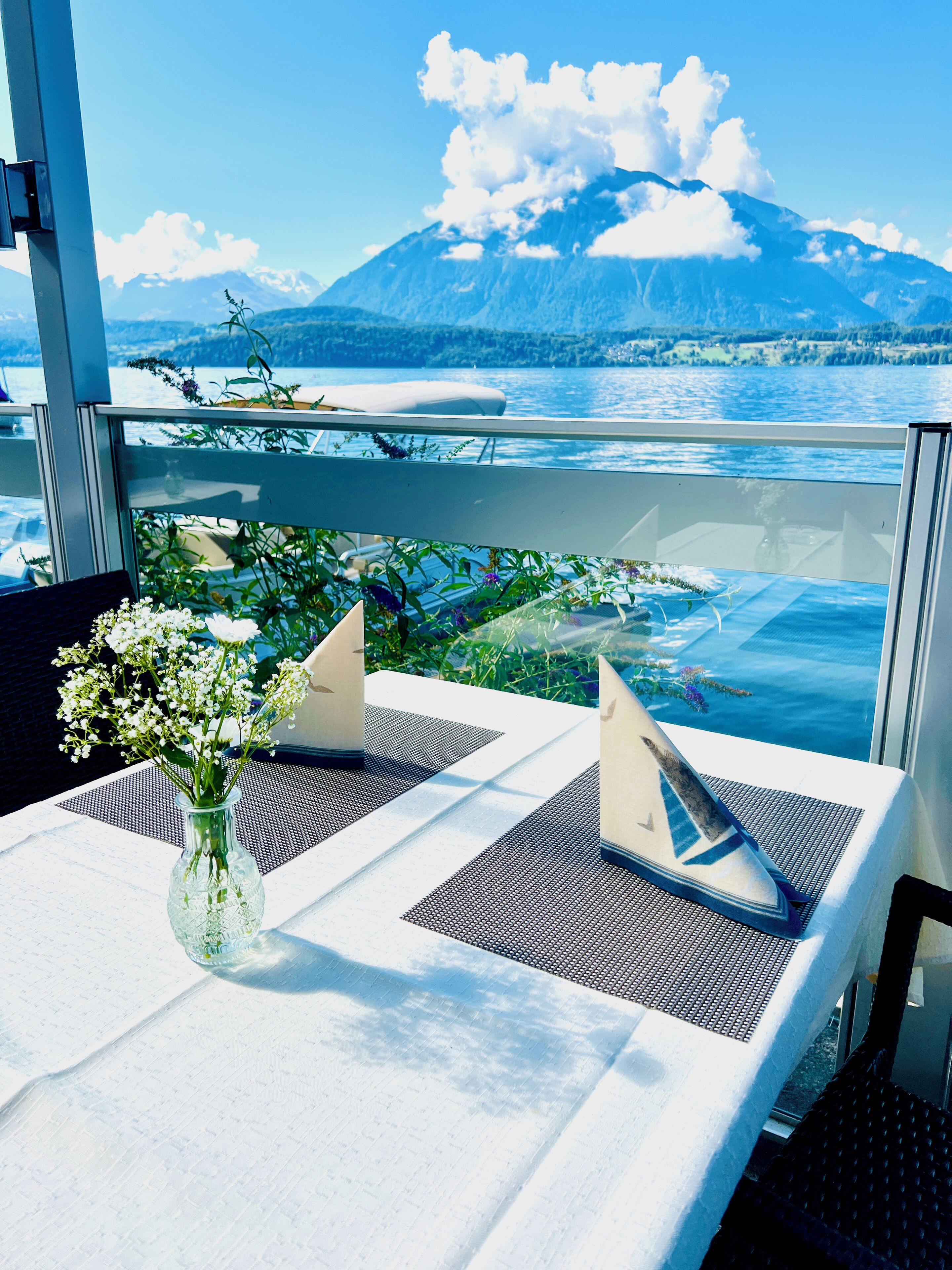 Una mesa con un florero, dos servilletas y vistas a una montaña y al agua.