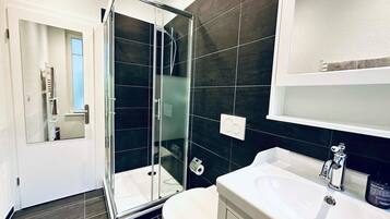Un baño moderno con cabina de ducha de vidrio, inodoro blanco y lavabo blanco con espejo arriba.