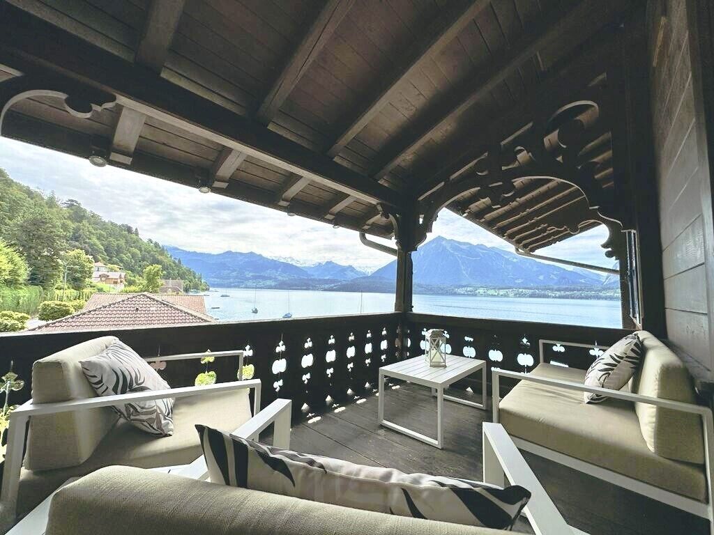 A balcony with outdoor seating, a view of a lake and mountains, and a wooden ceiling.