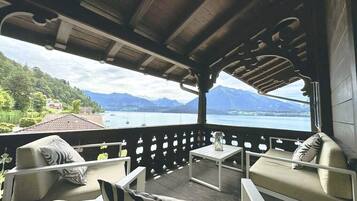A balcony with outdoor seating, a view of a lake and mountains, and a wooden ceiling.
