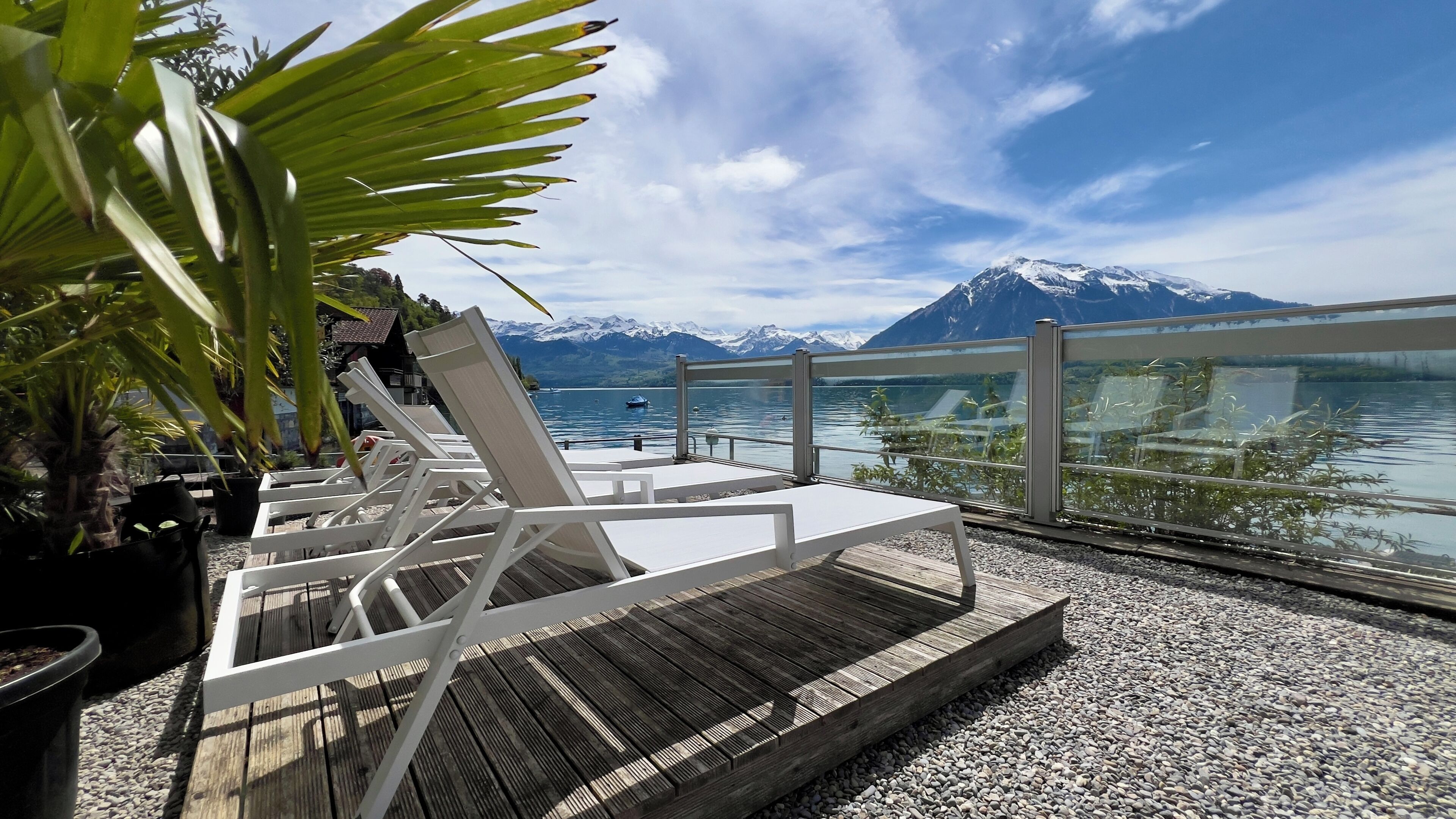 Une terrasse en bois avec des chaises longues blanches, donnant sur un lac et offrant une vue sur des montagnes en arrière-plan.