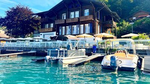 A wooden building with balconies, a dock with boats, and a clear sky. - Boutique Hotel Niesenblick Self Check In (Oberhofen am Thunersee)