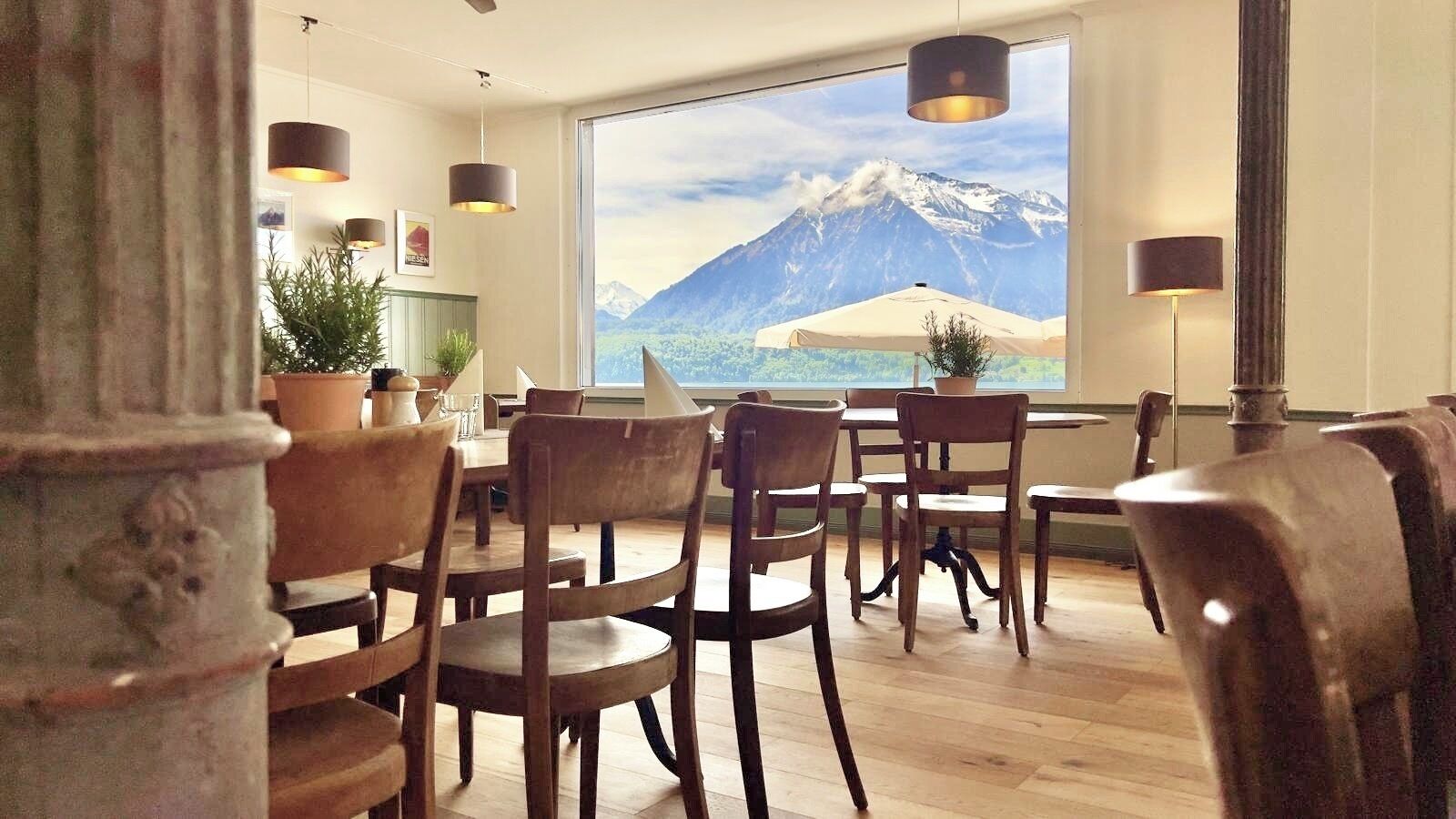 Un espace repas avec des chaises et des tables en bois, une grande fenêtre donnant sur les montagnes et des lampes suspendues.